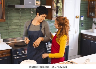 Happy biracial lesbian couple in aprons cooking, talking in kitchen. Cooking, food, gay, relationship, togetherness, domestic life and healthy lifestyle, unaltered. - Powered by Shutterstock