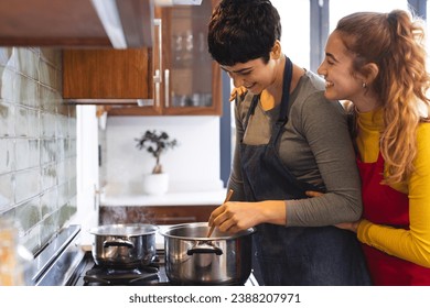 Happy biracial lesbian couple cooking on hob and embracing in kitchen, copy space. Love, cooking, food, gay, relationship, togetherness, domestic life and healthy lifestyle, unaltered. - Powered by Shutterstock