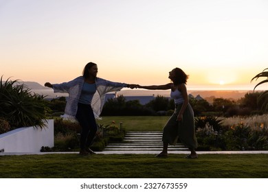 Happy biracial lesbian couple dancing in garden at sunset. Lifestyle, relationship, togetherness, nature and domestic life, unaltered. - Powered by Shutterstock