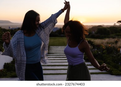 Happy biracial lesbian couple dancing in garden at sunset. Lifestyle, relationship, togetherness, nature and domestic life, unaltered. - Powered by Shutterstock