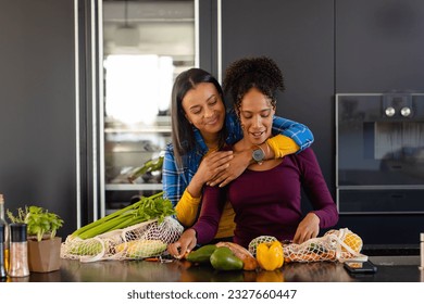 Happy biracial lesbian couple embracing and unpacking groceries in kitchen. Shopping, food, healthy lifestyle, lifestyle, relationship, togetherness and domestic life, unaltered. - Powered by Shutterstock