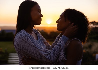 Happy biracial lesbian couple embracing in garden at sunset. Lifestyle, relationship, togetherness, nature and domestic life, unaltered. - Powered by Shutterstock