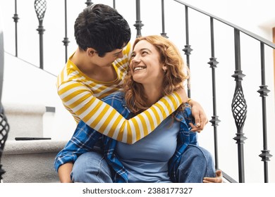 Happy biracial lesbian couple embracing sitting on stairs at home smiling. Free time, gay, love, relationship, togetherness, domestic life and lifestyle, unaltered. - Powered by Shutterstock