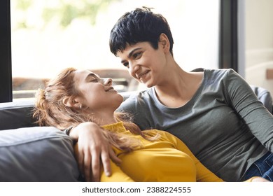 Happy biracial lesbian couple embracing on couch and smiling in sunny living room. Romance, love, relaxation, gay, relationship, togetherness, domestic life and lifestyle, unaltered. - Powered by Shutterstock