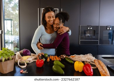 Happy biracial lesbian couple hugging and unpacking groceries in kitchen. Shopping, food, healthy lifestyle, lifestyle, relationship, togetherness and domestic life, unaltered. - Powered by Shutterstock