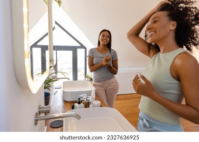 Happy biracial lesbian couple looking in mirrors in bathroom. Lifestyle, relationship, togetherness, self care and domestic life, unaltered. - Powered by Shutterstock