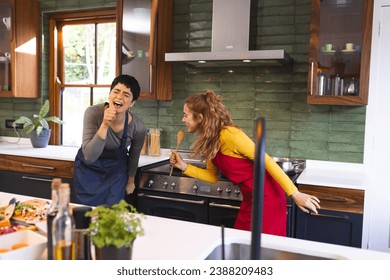 Happy biracial lesbian couple preparing meal having fun singing in kitchen. Fun, cooking, food, gay, relationship, togetherness, domestic life and healthy lifestyle, unaltered. - Powered by Shutterstock