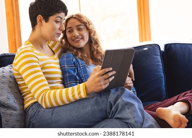 Happy biracial lesbian couple relaxing on couch using tablet together. Communication, free time, relaxation, relationship, togetherness, domestic life and lifestyle, unaltered. - Powered by Shutterstock