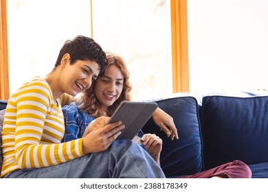 Happy biracial lesbian couple relaxing on couch using tablet together, copy space. Communication, free time, relaxation, relationship, togetherness, domestic life and lifestyle, unaltered. - Powered by Shutterstock