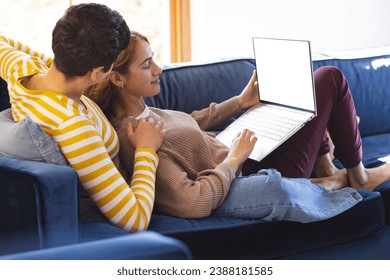 Happy biracial lesbian couple relaxing on couch using laptop together. Communication, free time, relaxation, relationship, togetherness, domestic life and lifestyle, unaltered. - Powered by Shutterstock