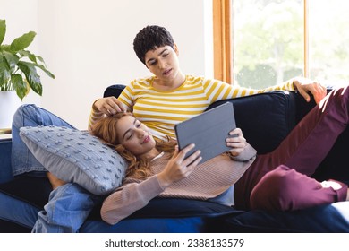 Happy biracial lesbian couple relaxing on couch together using tablet at home. Communication, gay, love, relationship, togetherness, domestic life and lifestyle, unaltered. - Powered by Shutterstock