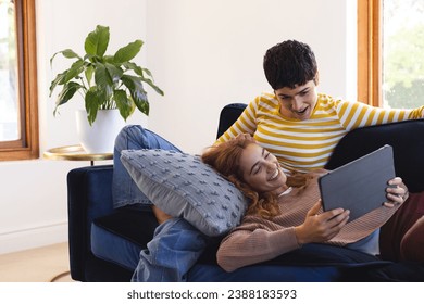 Happy biracial lesbian couple relaxing on couch together using tablet at home, copy space. Communication, gay, relationship, togetherness, domestic life and lifestyle, unaltered. - Powered by Shutterstock