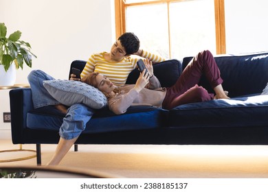 Happy biracial lesbian couple relaxing on couch together using smartphones at home. Communication, gay, relationship, togetherness, domestic life and lifestyle, unaltered. - Powered by Shutterstock