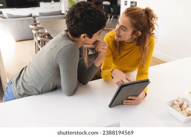 Happy biracial lesbian couple using tablet, standing leaning on countertop in sunny kitchen. Communication, gay, relationship, togetherness, domestic life and lifestyle, unaltered. - Powered by Shutterstock