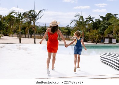 Happy biracial mother and daughter walking and holding hands by the swimming pool. Spending quality time, lifestyle, family, summertime and vacation concept. - Powered by Shutterstock