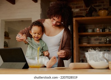 Happy biracial mother and daughter whisking egg near digital tablet in kitchen at home - Powered by Shutterstock