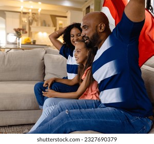 Happy biracial parents and daughter sitting on couch watching tv holding french flag and cheering. Family, sport, patriotism, celebration, togetherness, lifestyle and domestic life, unaltered. - Powered by Shutterstock