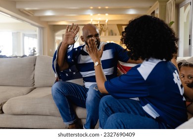 Happy biracial parents and daughter sitting on couch with american flag high fiving and smiling. Family, sport, patriotism, celebration, togetherness, lifestyle and domestic life, unaltered. - Powered by Shutterstock