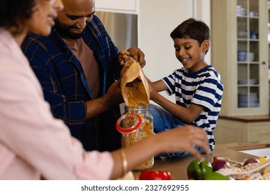 Happy biracial parents and son unpacking groceries and pouring pasta into storage jar in kitchen. Food, shopping, healthy lifestyle, ecology, family and domestic life, unaltered. - Powered by Shutterstock