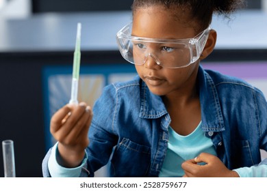 Happy biracial schoolgirl in safety glasses observing pipette in science class with copy space. Education, inclusivity, childhood, elementary school and learning concept. - Powered by Shutterstock