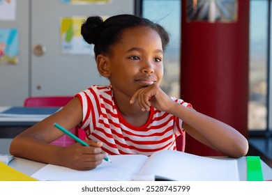 Happy biracial schoolgirl sitting at desk and learning in classroom at elementary school. Education, childhood, development, learning and elementary school, unaltered. - Powered by Shutterstock