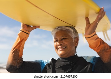 Happy biracial senior woman carrying yellow surfboard over head at beach during sunny day. water sport and active lifestyle. - Powered by Shutterstock