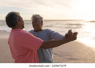 Happy biracial senior woman enjoying romantic dance with man at beach during sunset. lifestyle, love and weekend. - Powered by Shutterstock