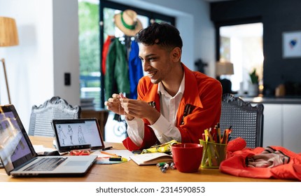 Happy biracial transgender fashion designer holding thread, using laptop and tablet. Gender, fashion, design, communication and lifestyle, unaltered. - Powered by Shutterstock