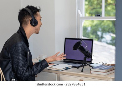 Happy biracial transgender man in headphones, using laptop, talking to microphone while podcasting. Gender, communication, lifestyle, social media and domestic life, unaltered. - Powered by Shutterstock