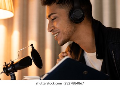 Happy biracial transgender man in headphones, making notes and talking to microphone, podcasting. Gender, communication, lifestyle, social media and domestic life, unaltered. - Powered by Shutterstock