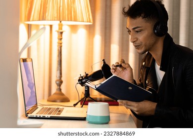 Happy biracial transgender man in headphones, making notes and talking to microphone, podcasting. Gender, communication, lifestyle, social media and domestic life, unaltered. - Powered by Shutterstock