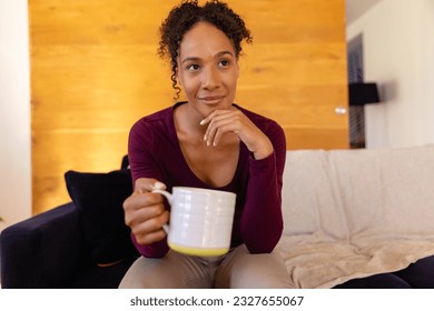 Happy biracial woman with cup of coffee making video call in living room. Lifestyle, communication and domestic life, unaltered. - Powered by Shutterstock