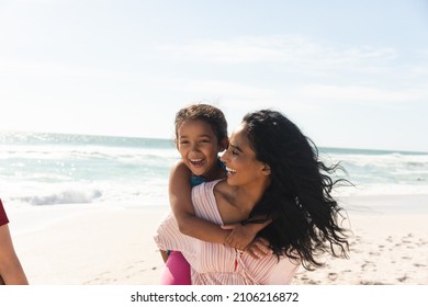 Happy biracial woman giving piggyback ride to daughter at beach against sky with copy space. family, lifestyle and weekend. - Powered by Shutterstock