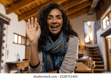 Happy biracial woman having video call and waving to camera in living room. Lifestyle, communication and domestic life, unaltered. - Powered by Shutterstock