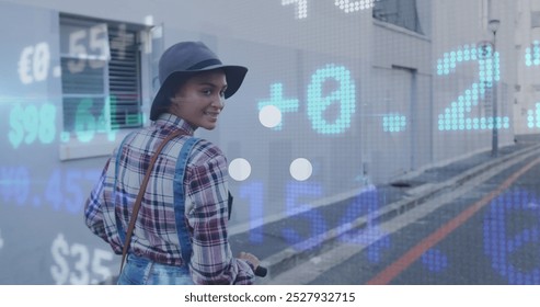 A happy biracial woman is out and about in the city on a sunny day, wearing a hat and riding on an electric scooter she looks back at the camera and smiles as she enjoys the beautiful day. - Powered by Shutterstock