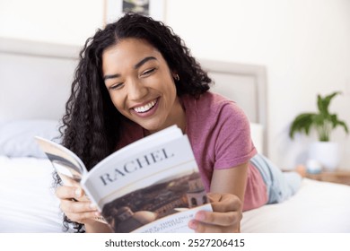 Happy biracial woman reading book lying on bed at sunny home. Lifestyle, free time and domestic life, unaltered. - Powered by Shutterstock