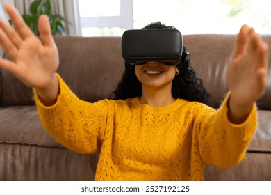 Happy biracial woman using vr headset at home. Lifestyle, free time, communication, virtual reality and domestic life, unaltered. - Powered by Shutterstock