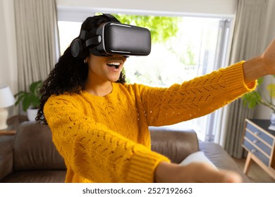 Happy biracial woman using vr headset at home. Lifestyle, free time, communication, virtual reality and domestic life, unaltered. - Powered by Shutterstock