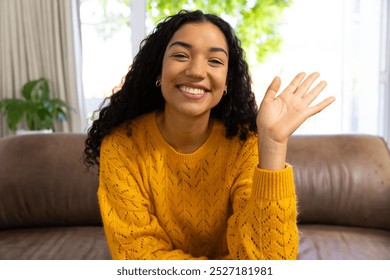 Happy biracial woman in yellow sweater making video call and waving at home. Lifestyle, free time, communication and domestic life, unaltered. - Powered by Shutterstock