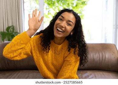 Happy biracial woman in yellow sweater making video call and waving at home. Lifestyle, free time, communication and domestic life, unaltered. - Powered by Shutterstock