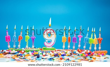 Happy birthday candle letters with number nine on a beautiful blue background. Copy space Happy birthday greetings for 9 years old child, lit candles with holiday decorations