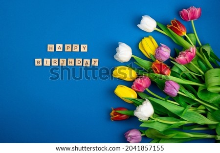 Happy birthday card. Wooden letters. Mix of spring tulips flowers. Background with flowers tulips close-up different colors. Multi-colored spring flower. Gift. Red, pink, white and yellow tulip
