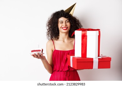 Happy birthday girl in red dress, celebrating and holding gifts with bday cake, standing on white background