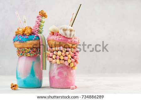 Happy Birthday party background: Two freak shakes topping with donut, marshmallow, meringues, popcorn and marmalade over grey background with copy space; selective focus. 