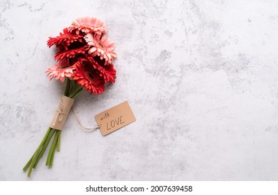 Happy birthday. Red gerbera daisy flowers and craft label tag with words With Love on concrete table, flat lay - Powered by Shutterstock