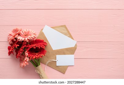 Happy birthday. Red gerbera daisy flowers, envelope and blank label tag on pink wooden table - Powered by Shutterstock