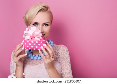 Happy Birthday. Sweet Blonde Woman Holding Small Gift Box With Ribbon. Soft Colors. Studio Portrait Over Pink Background