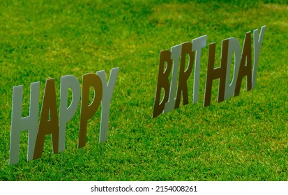 Happy Birthday Yard Sign For A Drive By Celebration. Different Color Letters Floating Against A Green Lawn Background. 