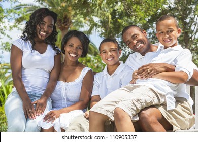 A Happy Black African American Family Of Two Parents And Three Children, Two Boys One Girl, Sitting Together Outside.