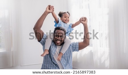 Happy black African American father daughter playing at home living room. Afro man carry piggyback little toddler girl. Cheerful family bonding together father’s day concept banner with copy space
